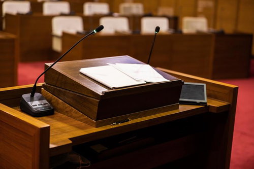 津山市議会議場の木製演壇に置かれた資料とマイクシステム
