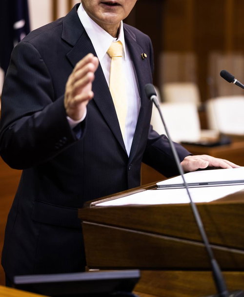 津山市議会の演壇で片手を上げながら演説する議員