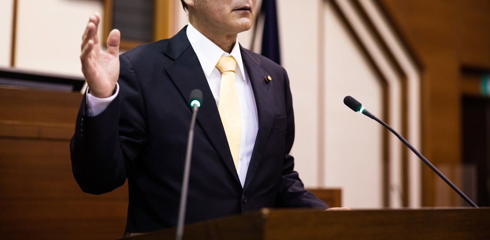 登壇席で右手を上げながら発言する紺色背広の議員
