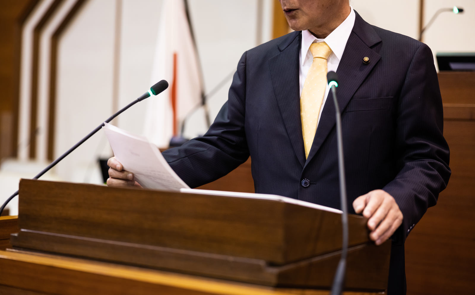紙の原稿を読みながら質問する男性議員と議場のマイク