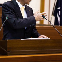 演壇で手を上げて発言する政治家の写真