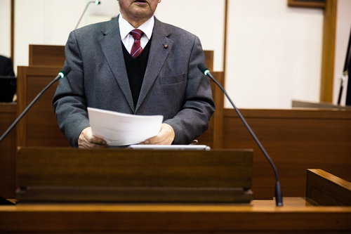 議場の演壇で書類を手に質問する男性議員の議会活動風景