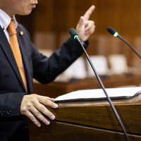 人差し指を立てて市議会で説明する議員の熱弁の写真