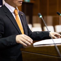 市議会で質問する議員の熱弁、黒いスーツの男性議員がマイクの前で発言の写真