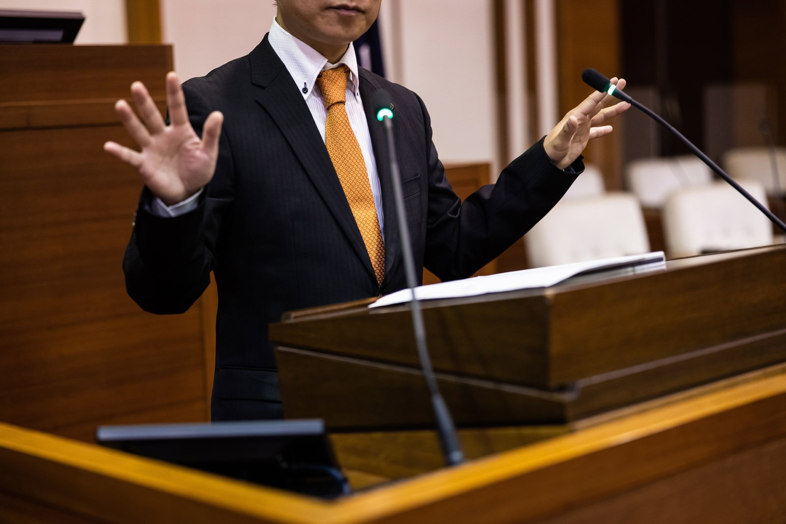 議場で両手のジェスチャーを交えながら登壇して発言する市議会議員
