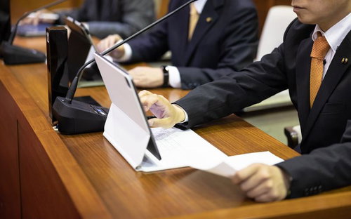 津山市議会の議員席でタブレットを操作しながら資料を確認する議員