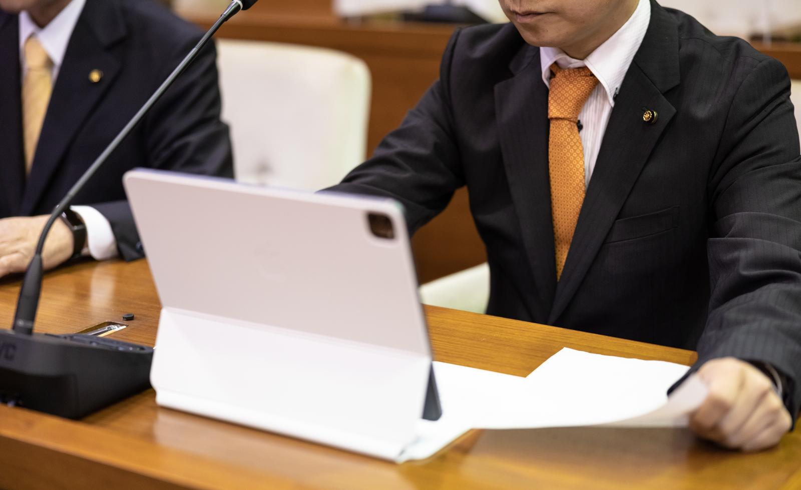 市議会の議場でタブレット端末を操作する黒いスーツの議員