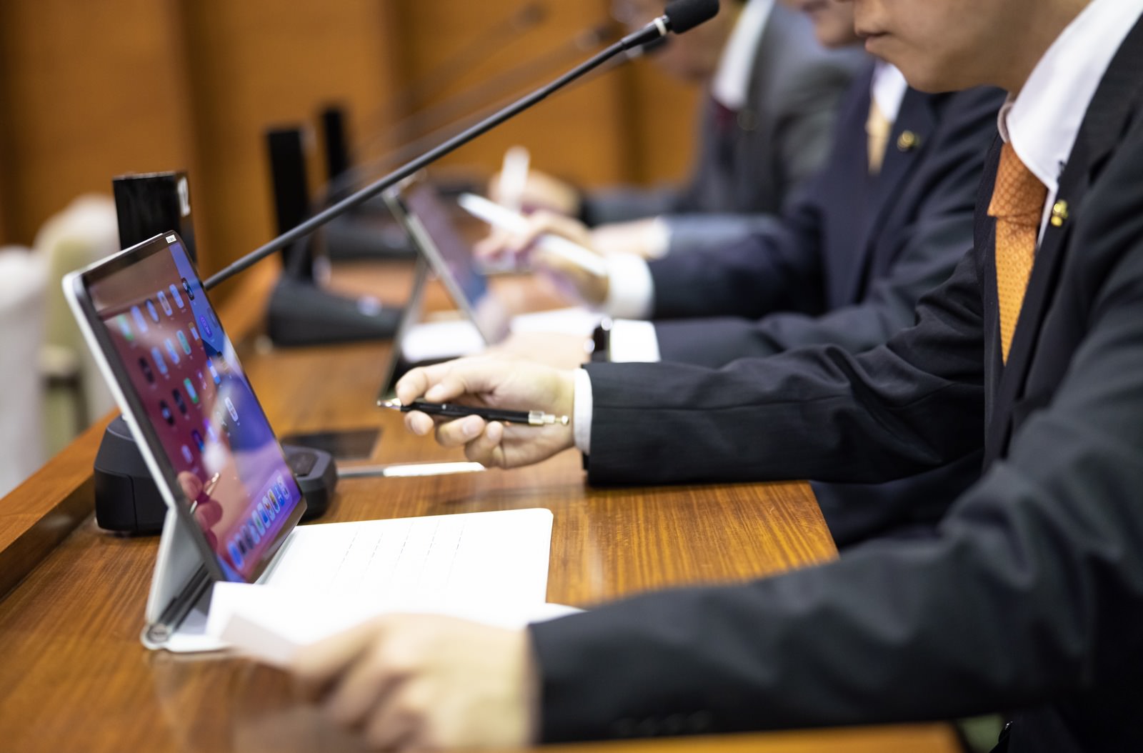 議会で資料を確認するタブレットを持つスーツ姿の男性議員