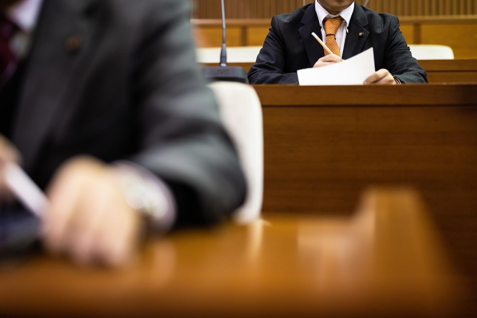 議員席で資料を確認する濃紺スーツの議員