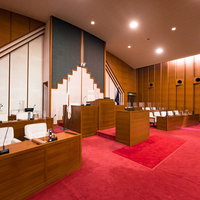 赤い絨毯敷きの木製議席が並ぶ現代的な議場の写真