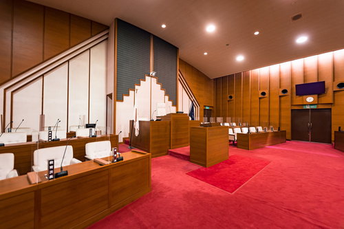 赤い絨毯敷きの木製議席が並ぶ現代的な議場