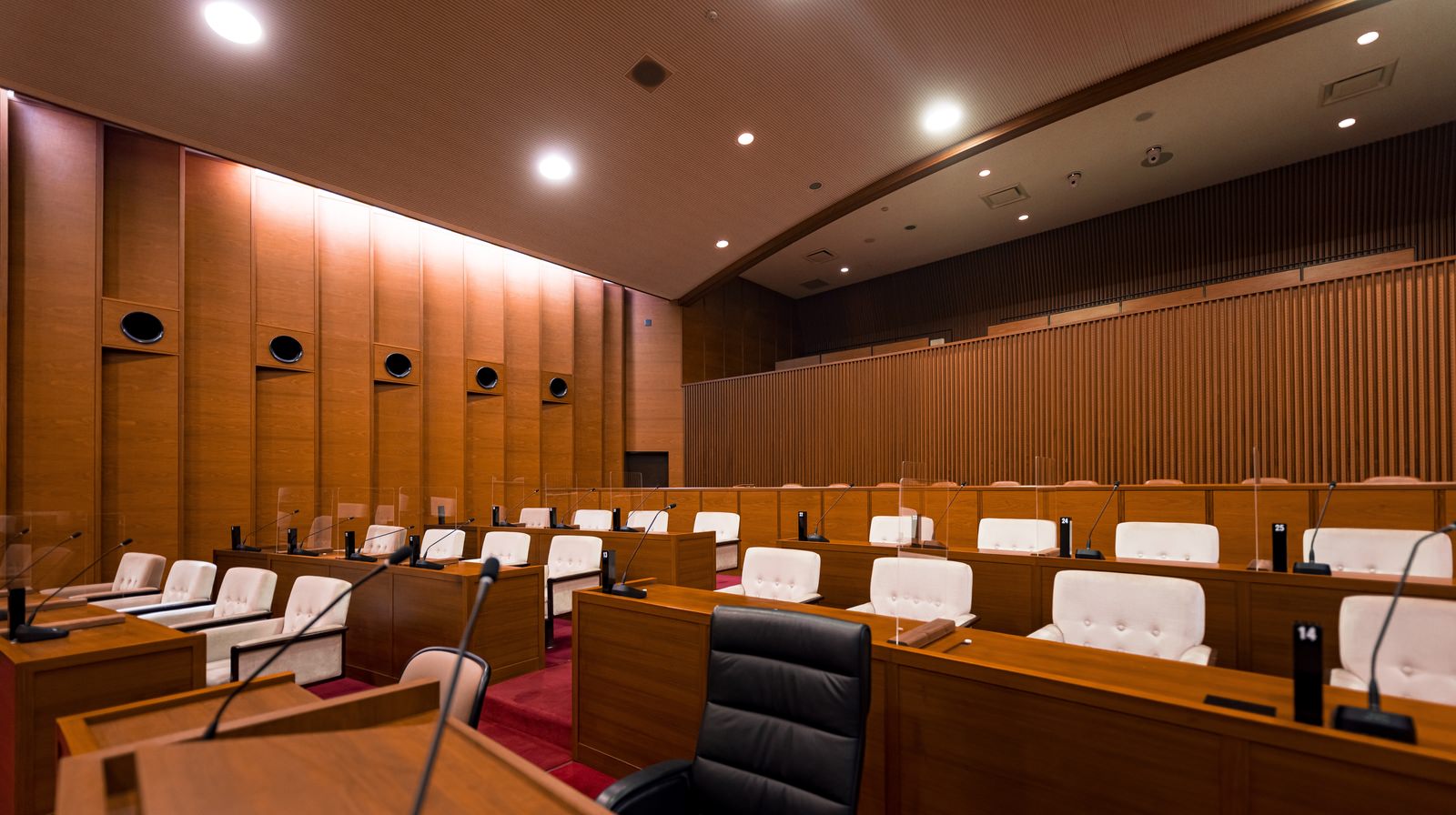 木製の議席と白いヘッドレストが並ぶ津山市議会の本会議場