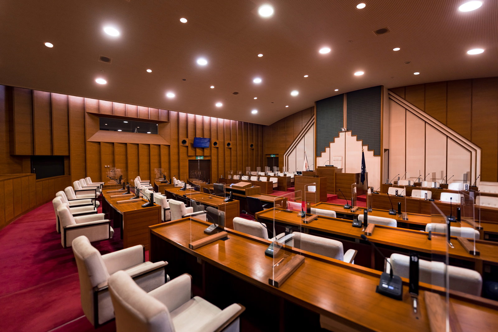 津山市議会の格調高い議場。木製パネルの壁と照明、赤いカーペット、議員席が配置されている