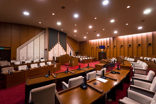 木製パネルと赤い絨毯が特徴の議場、議長席と議員席が並ぶ市議会