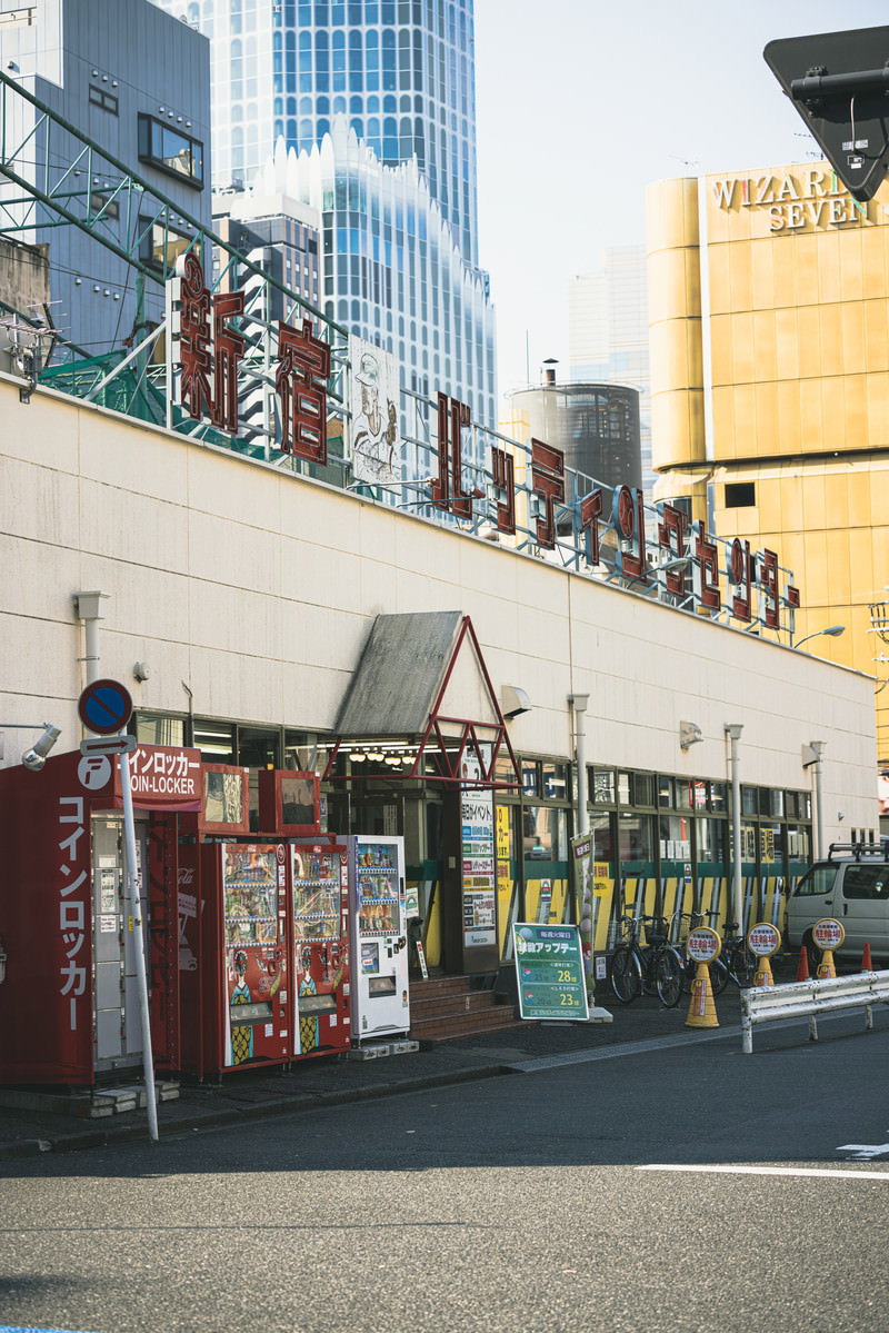 新宿のバッティングセンター前の路地裏風景、自動販売機と看板が並ぶ