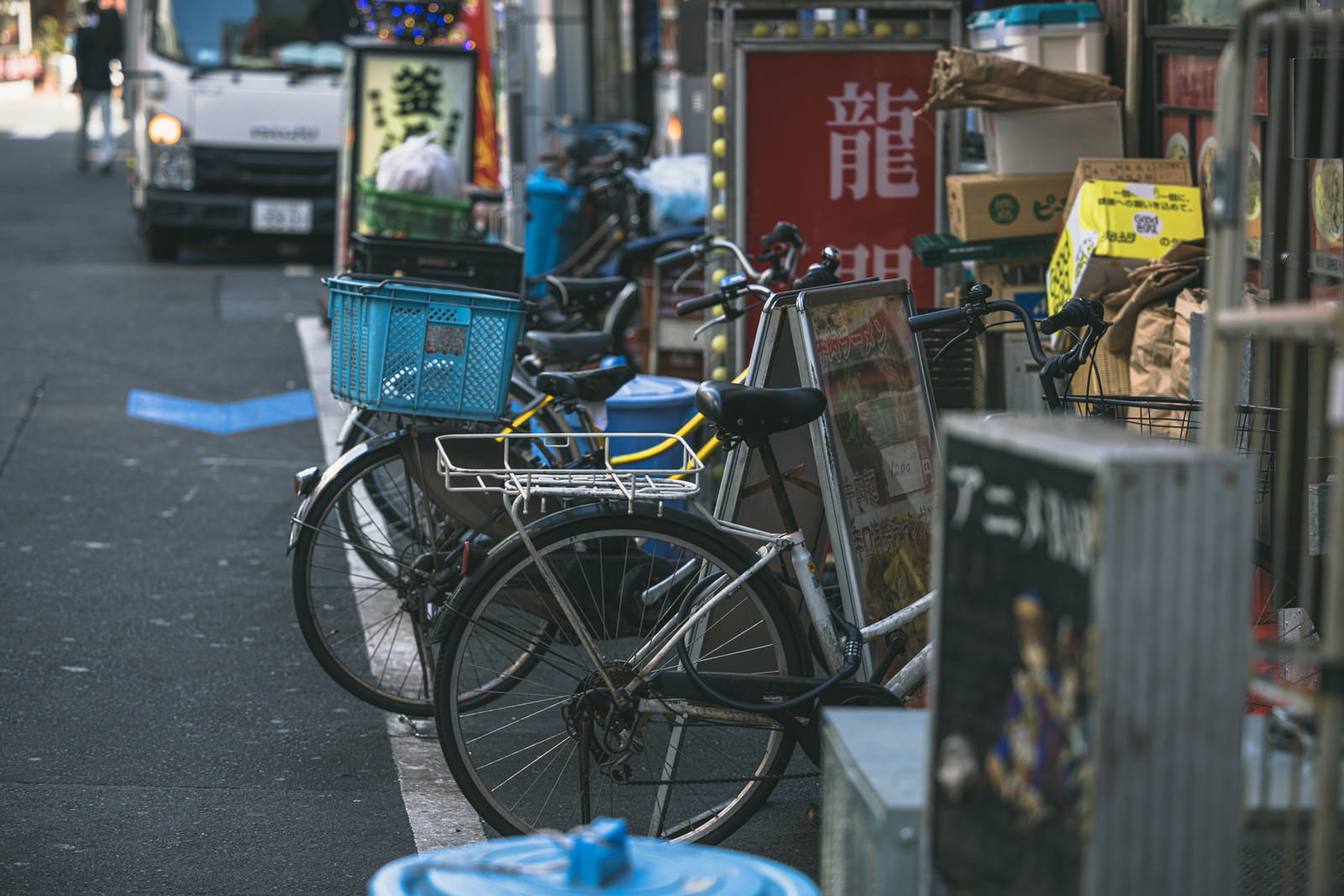 新宿の路地裏にある店先に青いカゴ付きの自転車が複数台並んでいる様子