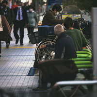 新宿の歩道脇の駐輪場に並ぶ自転車やバイクとベンチに座る人たちの写真