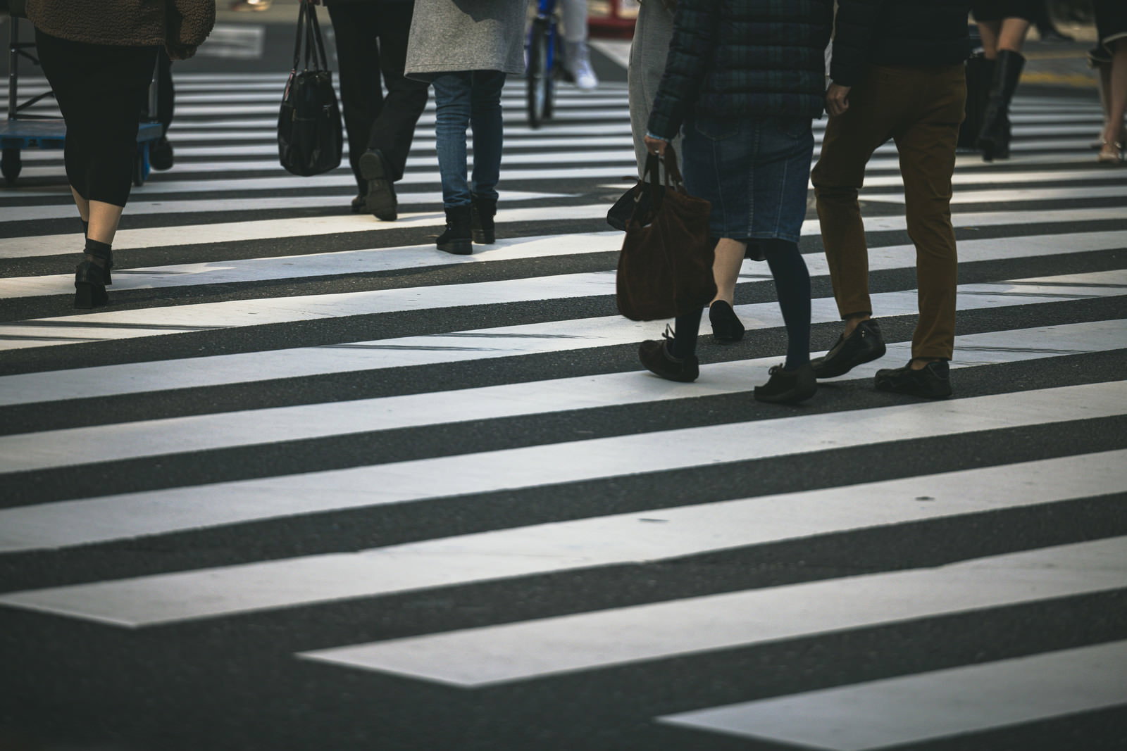 横断歩道の白い縞模様の上を歩く複数の人の足元