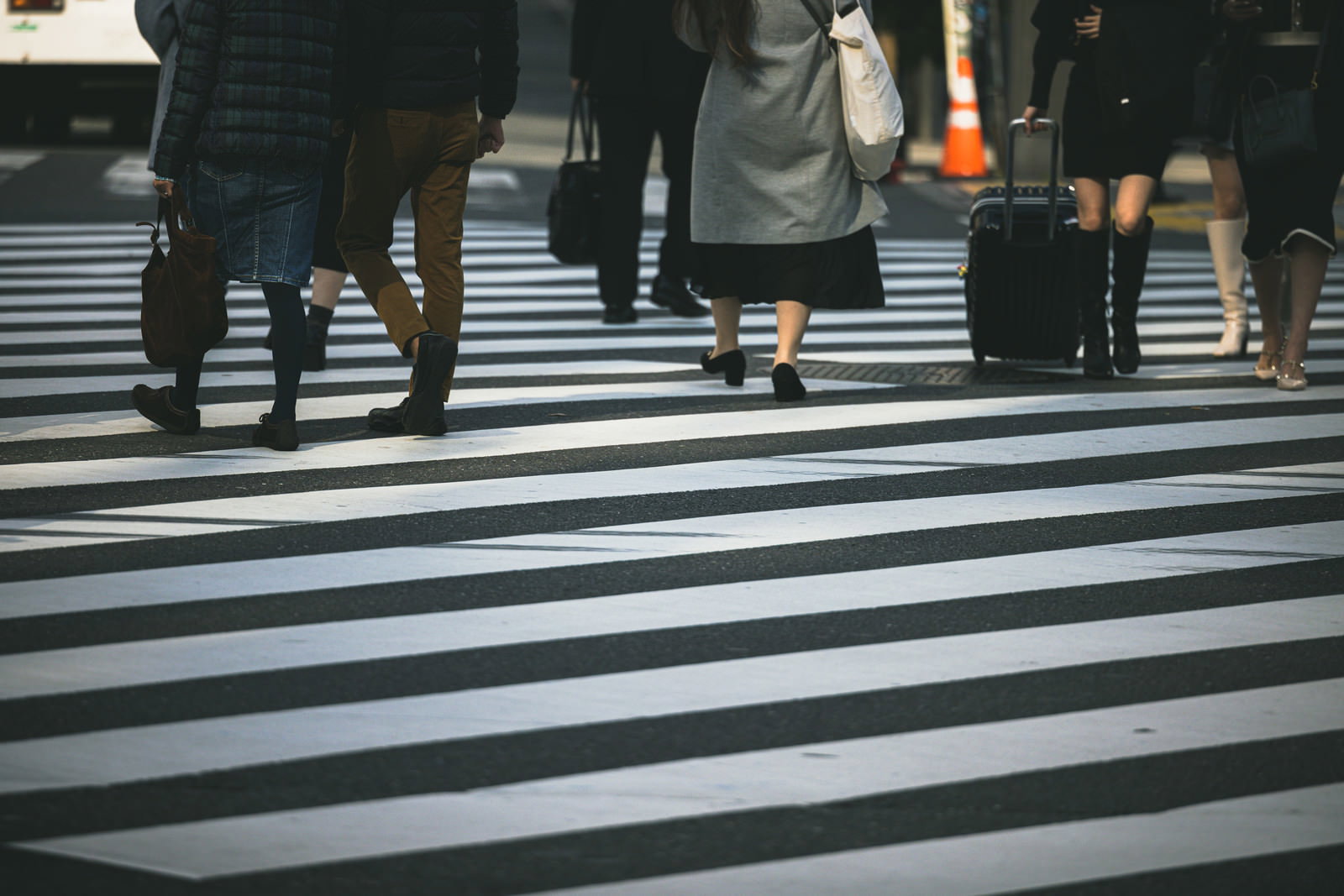 横断歩道の白線の上を歩く複数の人の足元を写した写真