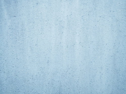 細かい斑点のシミが残る淡い青みのコンクリート壁