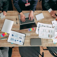 木目のテーブル上でグラフ資料を広げて会議する様子の写真