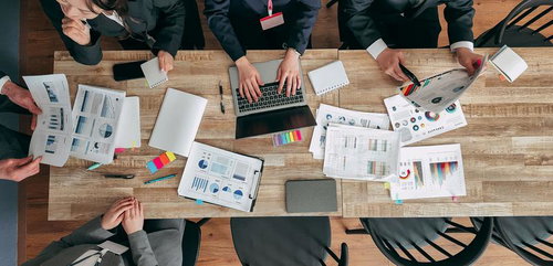 木目のテーブル上でグラフ資料を広げて会議する様子