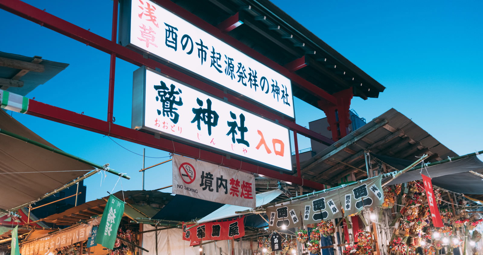 夜の鷲神社入口の看板と赤い提灯、奥に見える酉の市の屋台