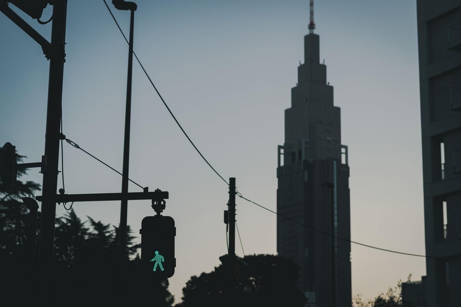 夕暮れ時の横断歩道で青信号が点灯し、背景にNTTドコモタワーのシルエットが見える風景