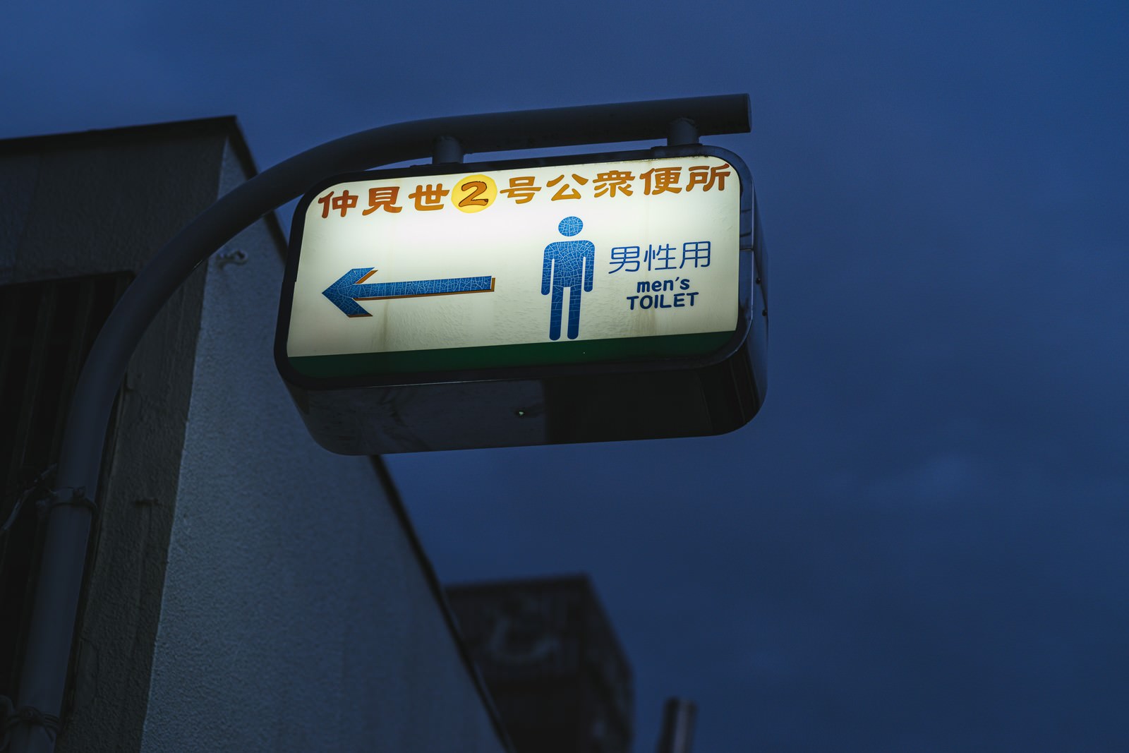 青い背景に白い男性のピクトグラムと左向きの矢印が描かれた公衆便所の案内看板