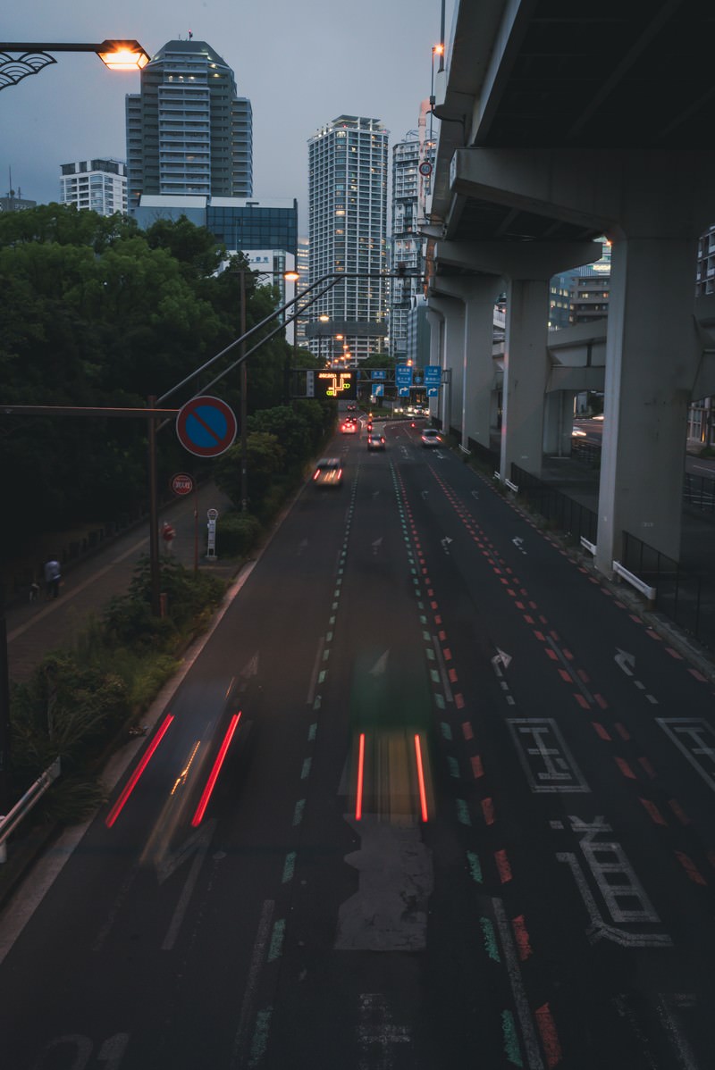 夜の国道で車のテールランプが描く赤い光跡とビル群