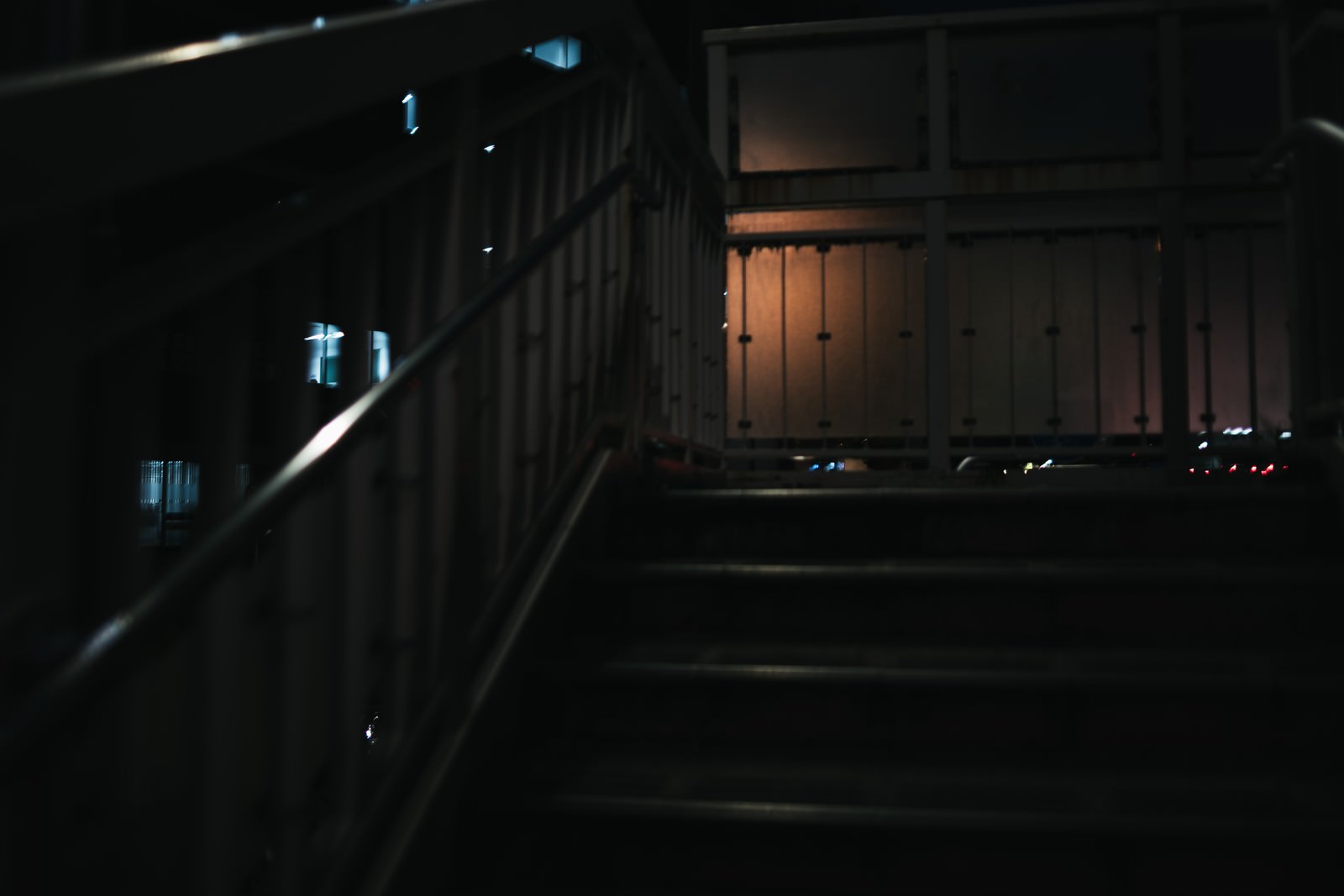 夜の歩道橋で街灯の明かりが目隠しを透して照らしている