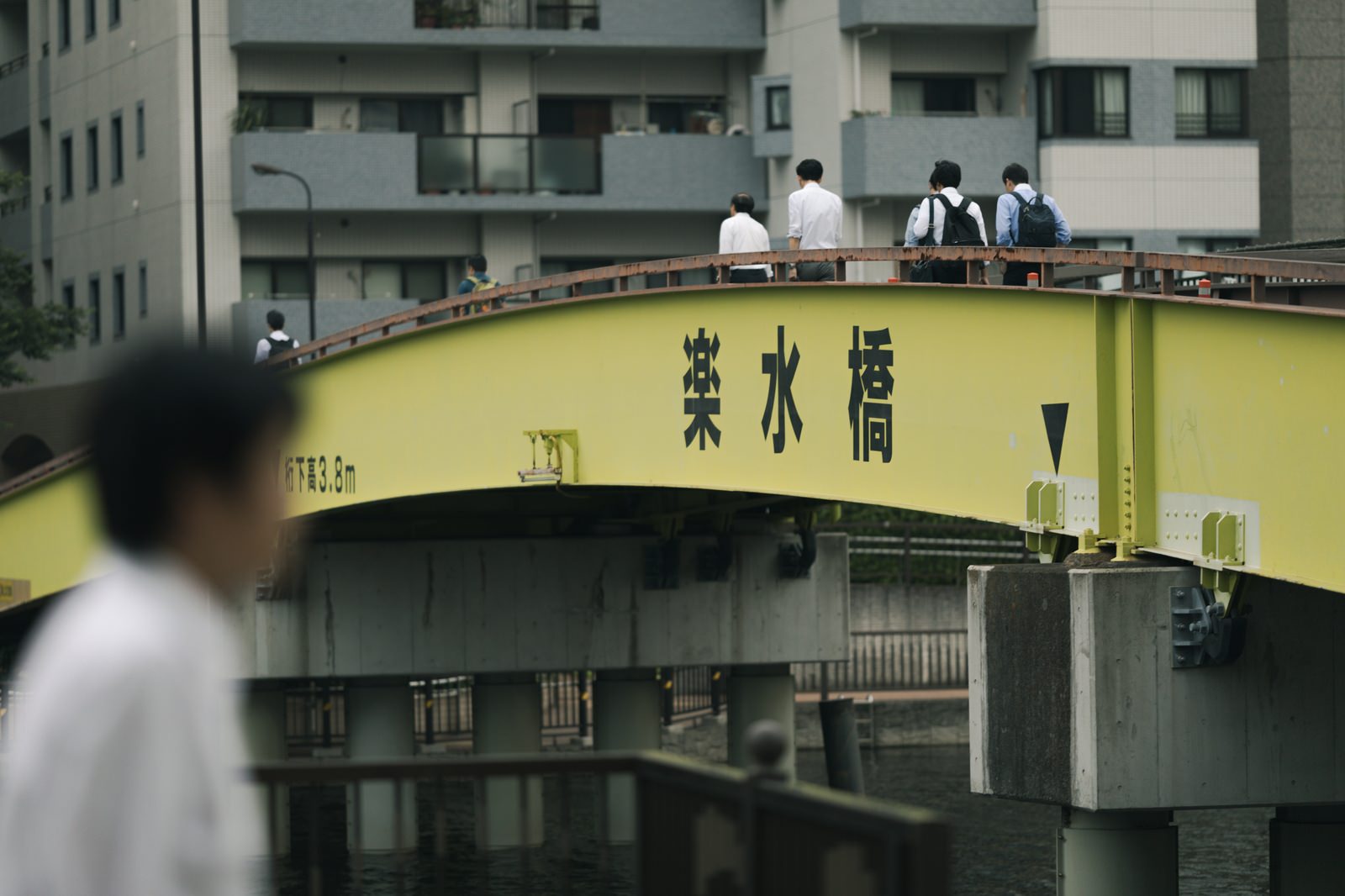 黄色いアーチ橋の楽水橋を歩く複数の人物と背景の高層マンション群