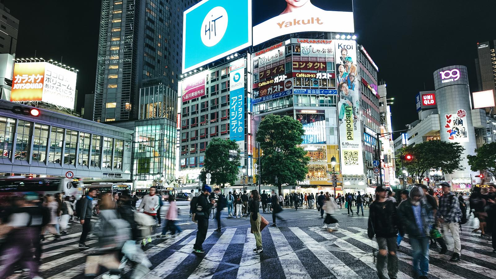 夜間の渋谷スクランブル交差点で大勢の人々が縞模様の横断歩道を横断している写真