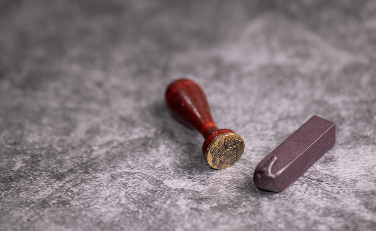 Sealing wax stamp and purple wax stick on gray surface