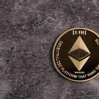 黒い石材の上で輝くETHロゴの金貨イーサリアムの写真