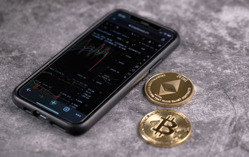 スマホのトレード画面と金貨（BTC・ETH）