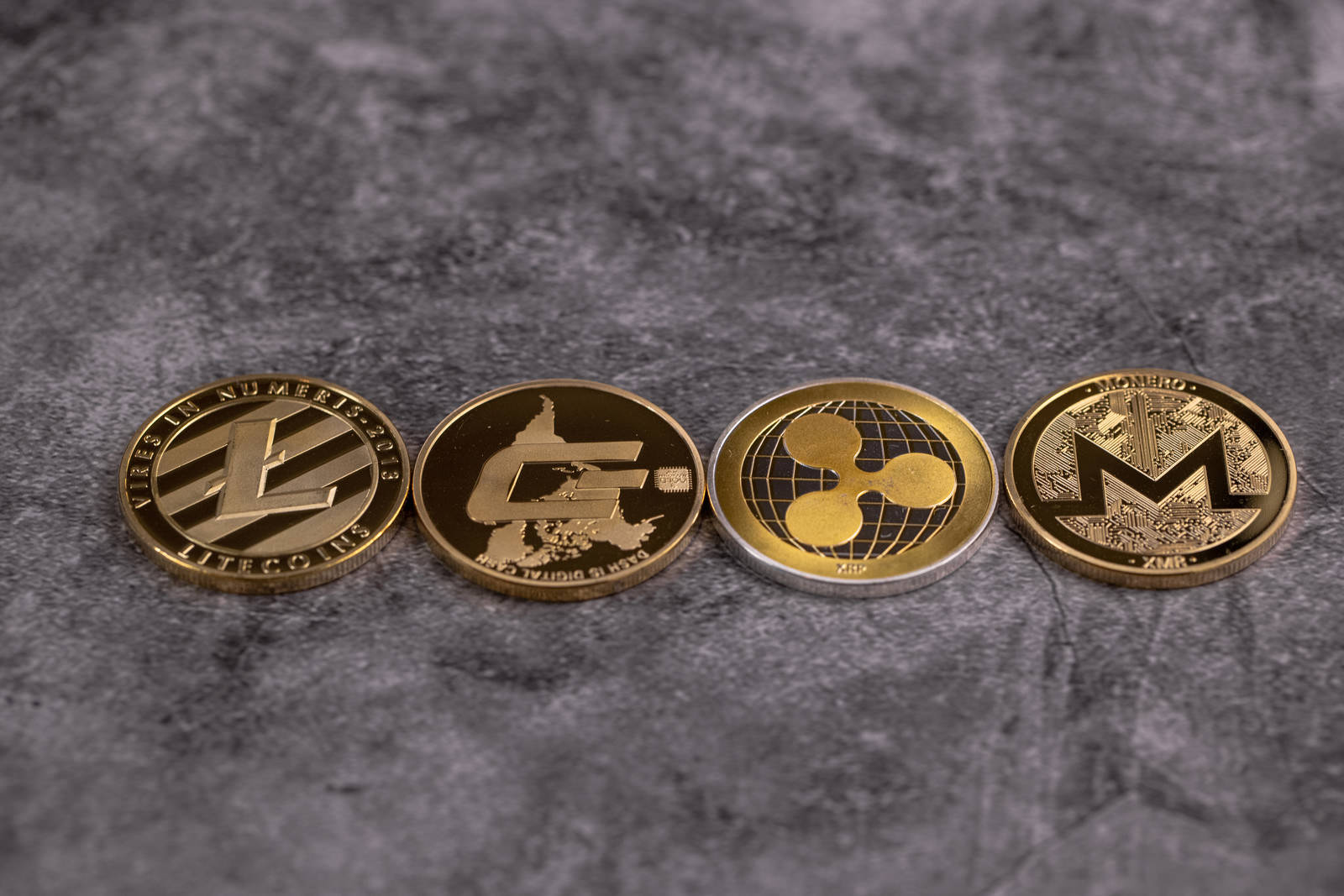 グレーの背景に一列に並ぶLTC、DASH、XRP、XMRの金貨