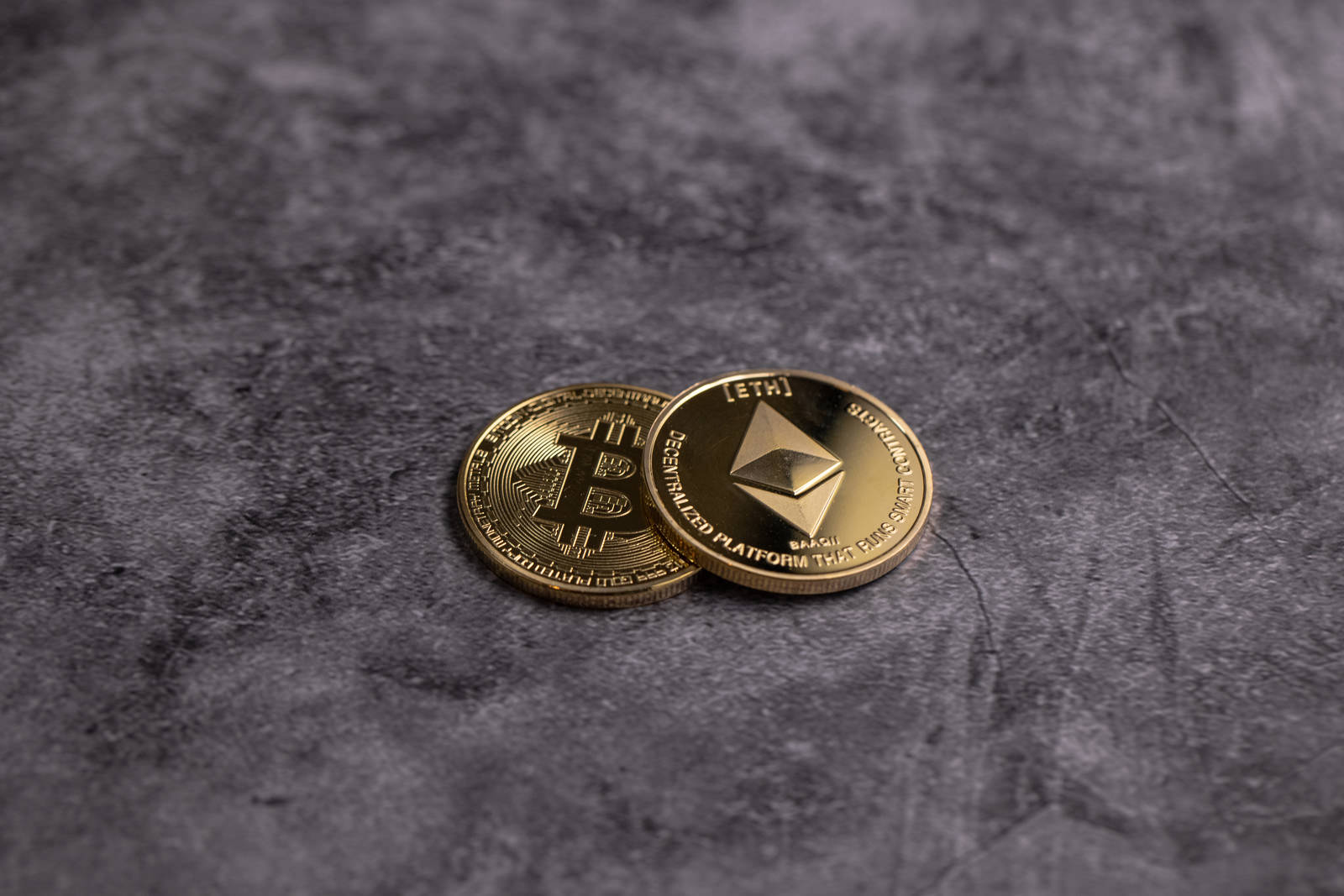 グレーの背景に重なり合って置かれた金色のビットコインとイーサリアムのコイン