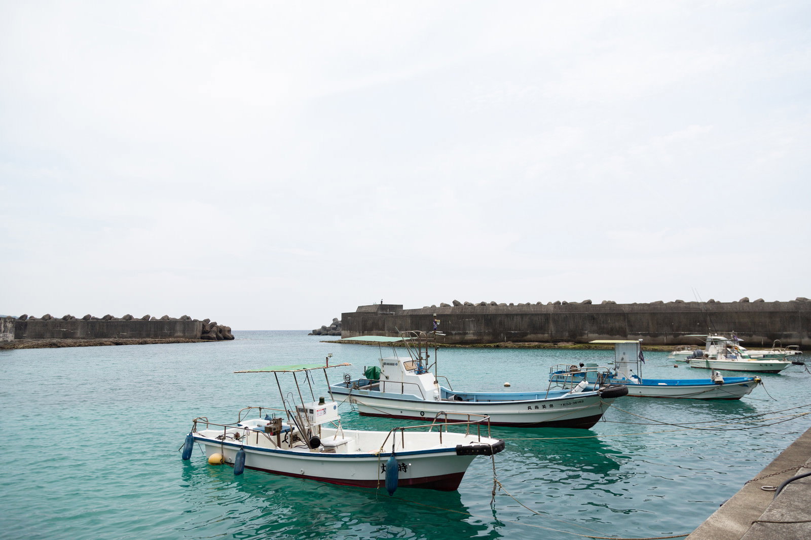堤防に停泊する白い漁船とエメラルドグリーンの海