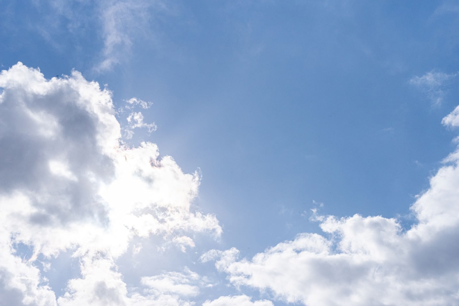 太陽が白い雲に隠れた青空と雲の間から差し込む日差し
