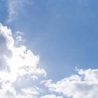 太陽が白い雲に隠れた青空と差し込む日差しの写真