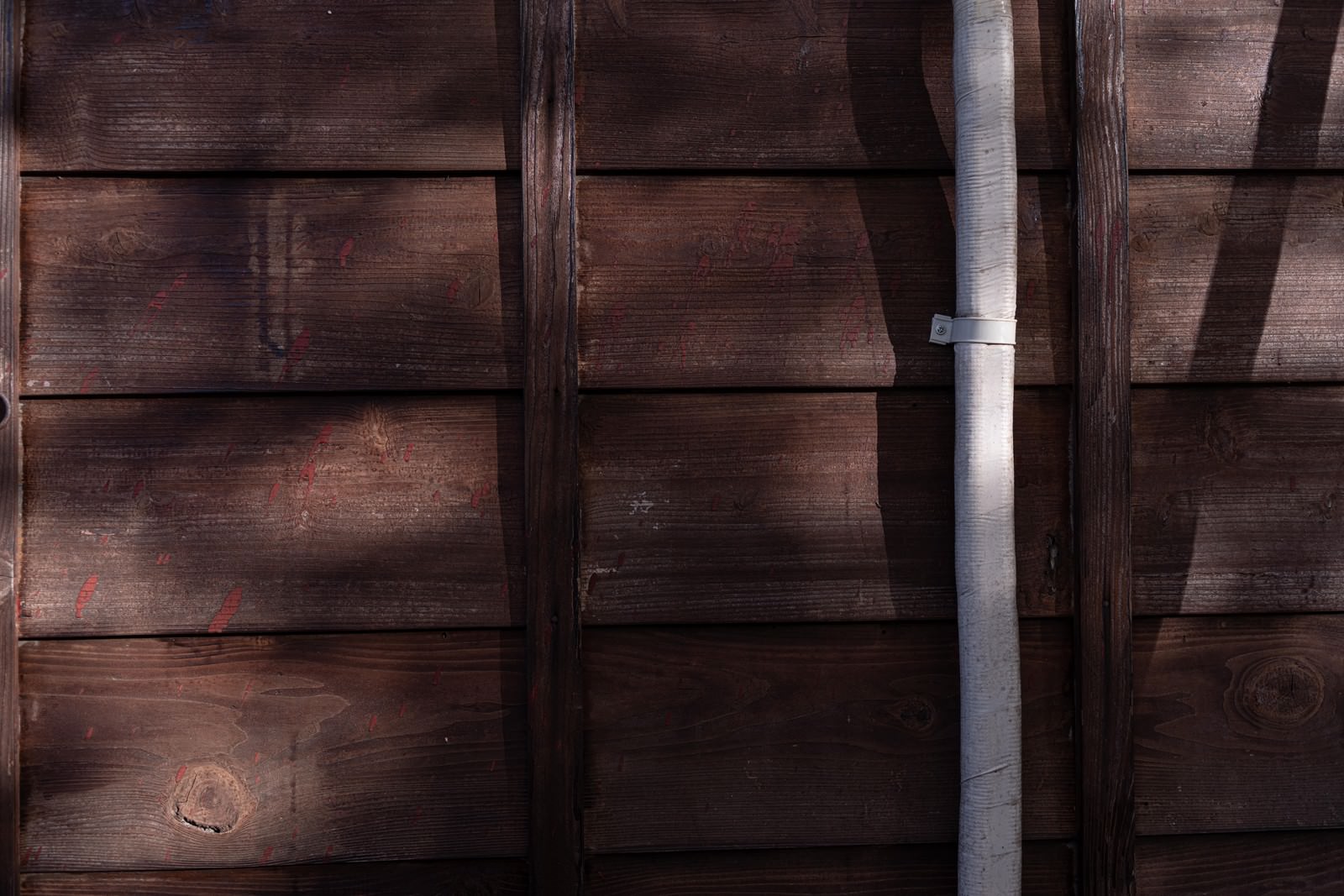 茶色の木目が見える板壁に白いドレンホースが縦に設置されている