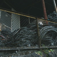 金網フェンス越しに見える雑に束ねられた廃ケーブルの写真