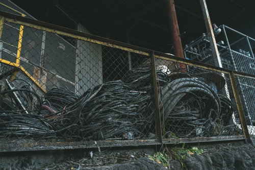 金網フェンス越しに見える雑に束ねられた廃ケーブル