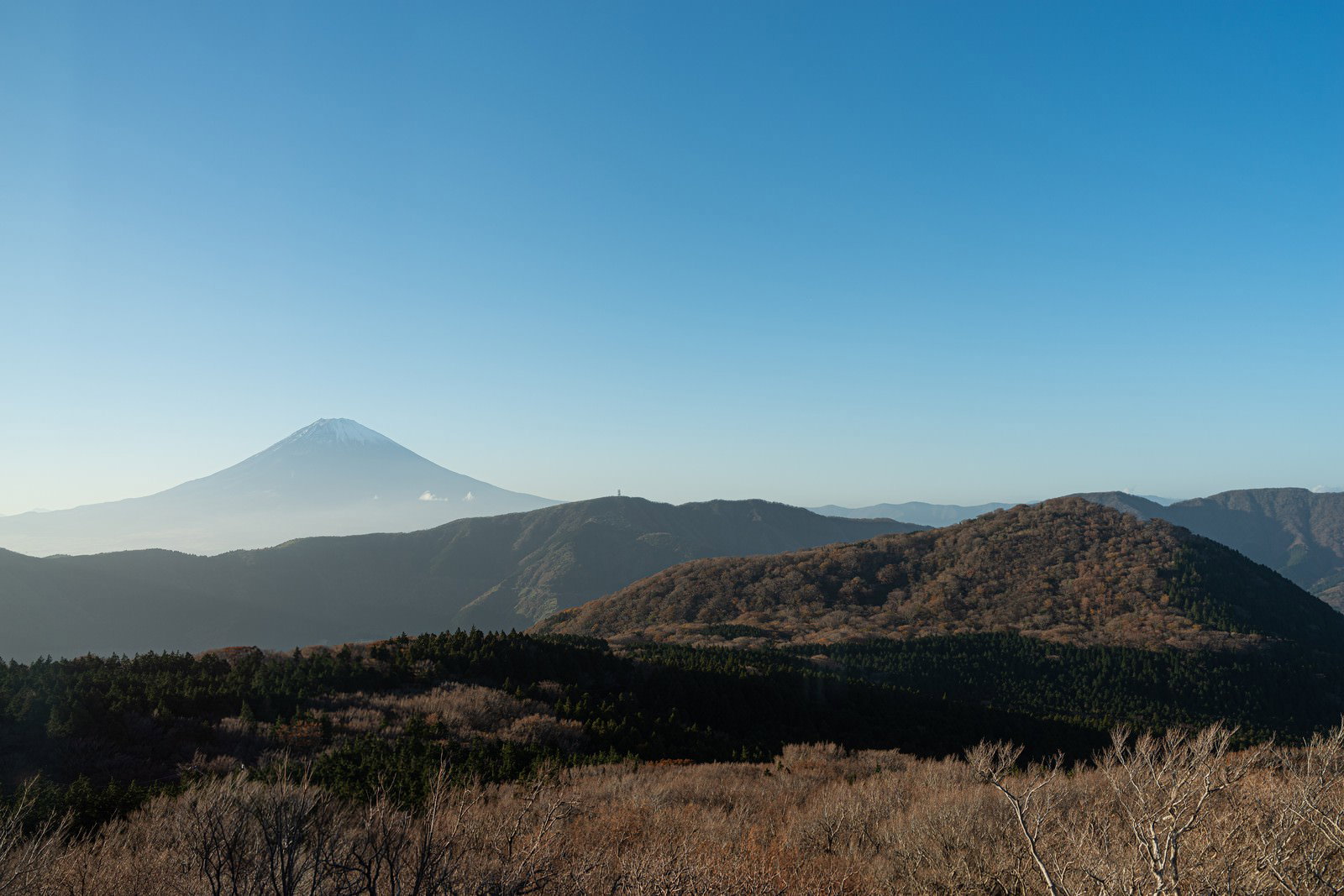 Hazy Mount Fuji and a range of mountains under a blue sky, with a foreground of brown grassland and hills