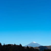 快晴の青空の下にくっきり見える富士山とシルエットの山々の写真