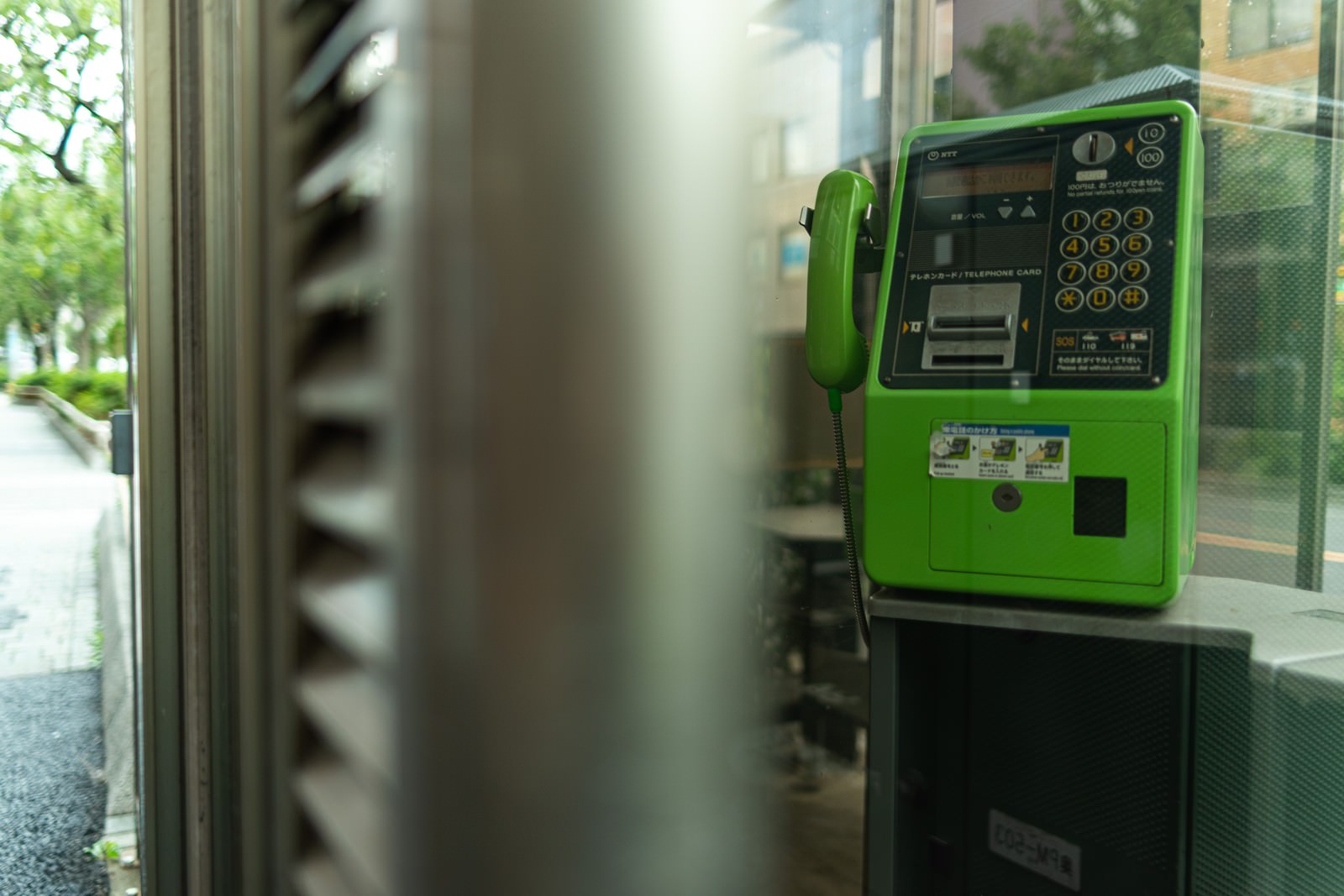 緑色の公衆電話ボックス内の電話機と街並みの背景