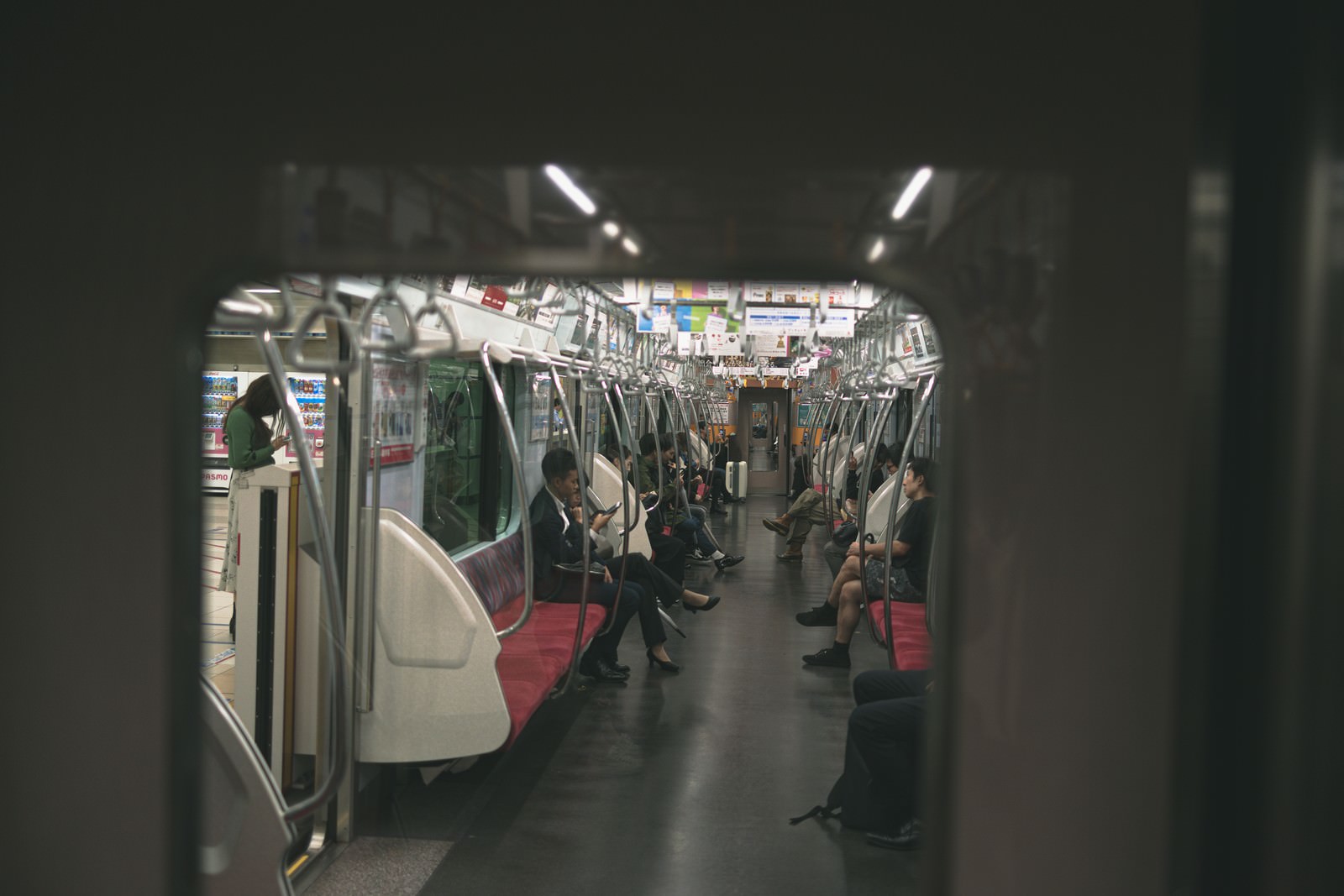 隣の車両から見た電車内の様子で複数の乗客が座席に座っている