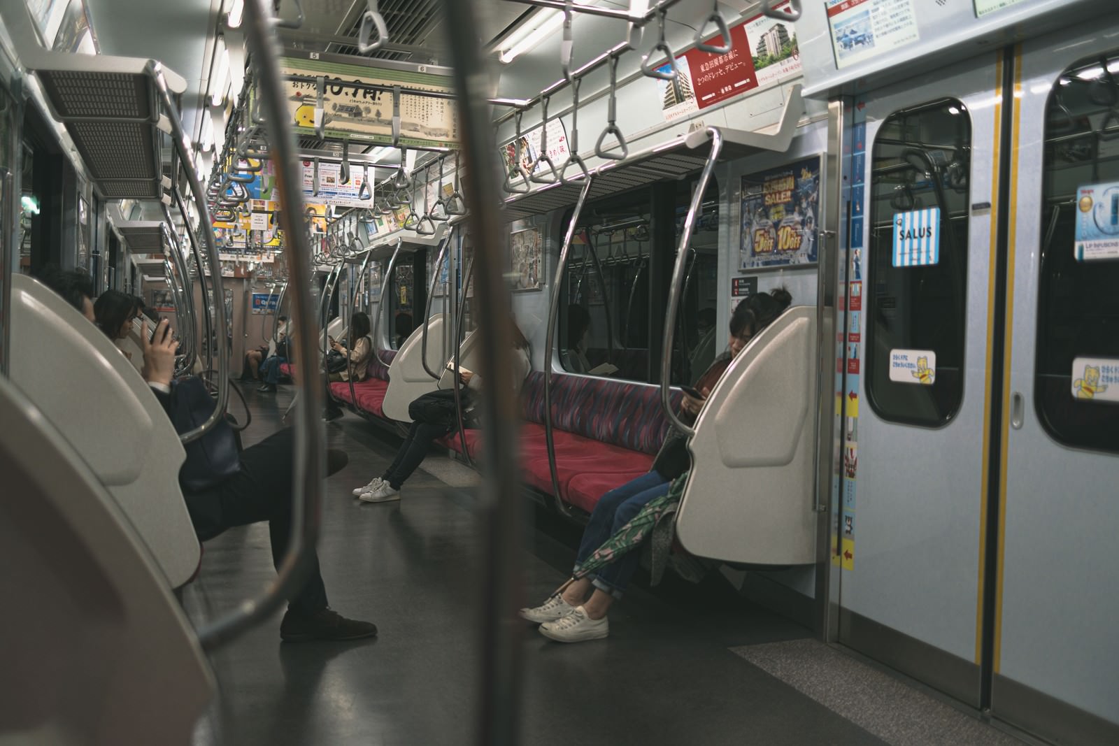 座席が空いた電車の車両内。赤いシートとつり革が見える