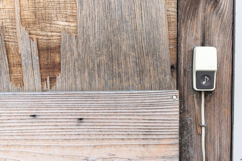 劣化したベニヤ壁に付いた白い玄関チャイム